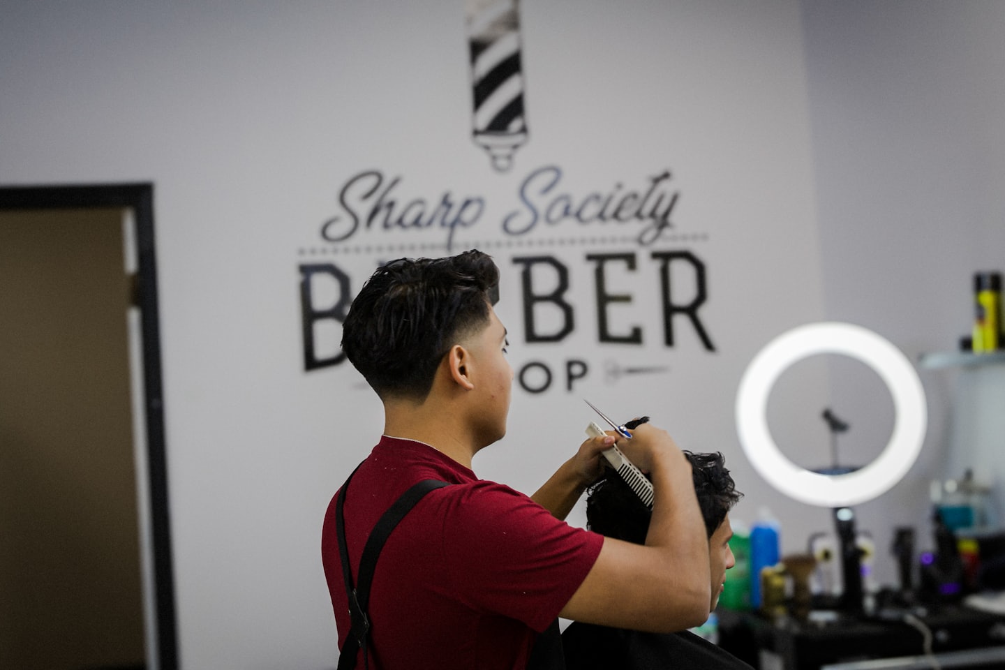 Un barbiere con grembiule bordeaux taglia i capelli a un cliente.