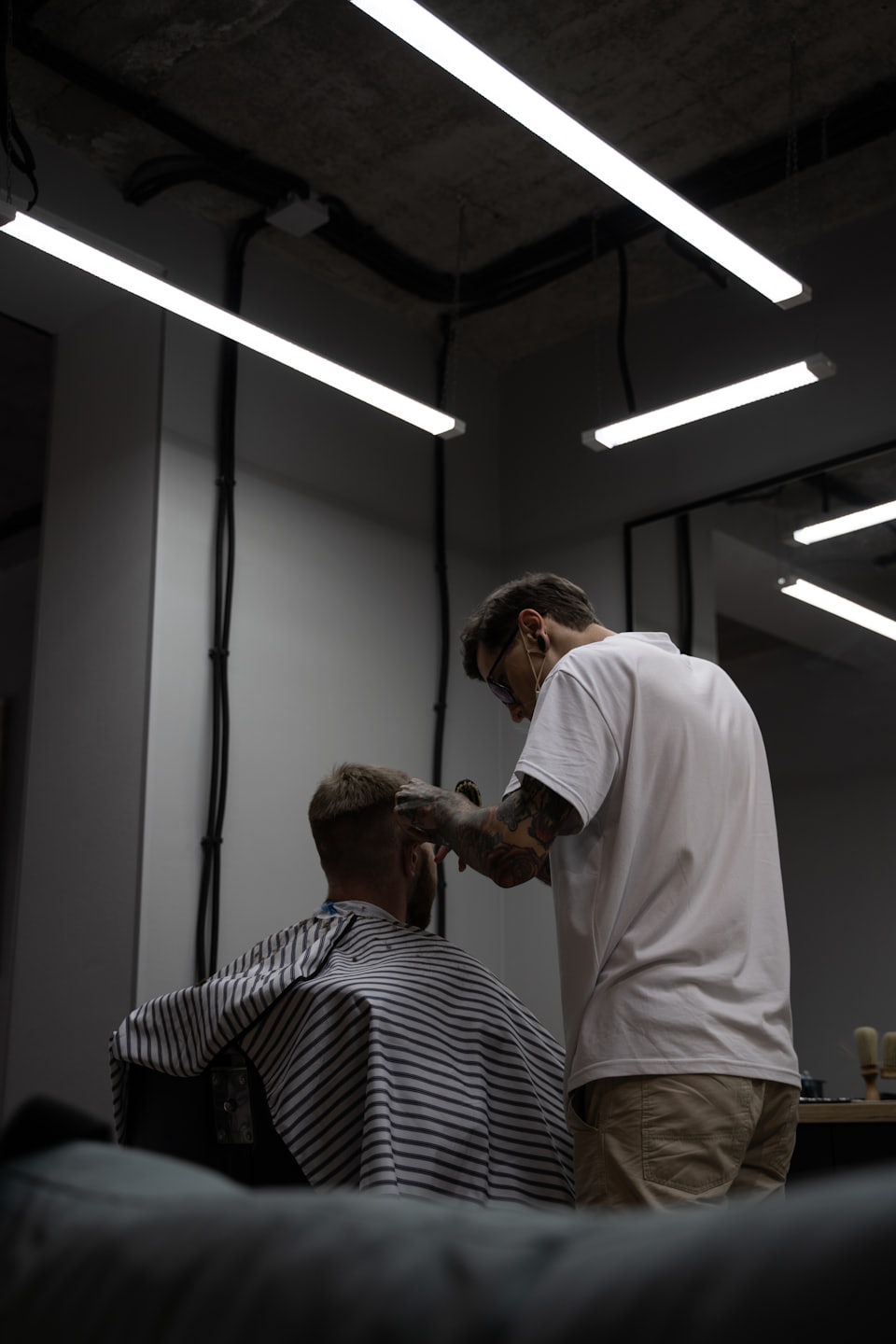 Un barbiere con braccia tatuate taglia i capelli a un cliente.