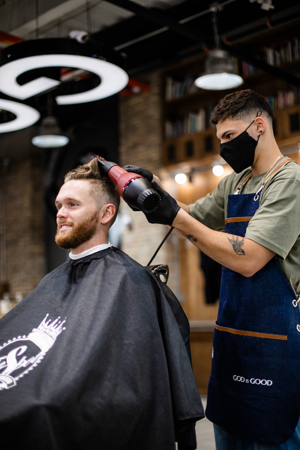 Barbiere che asciuga i capelli bagnati di un cliente con un asciugacapelli rosso e nero.